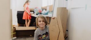 A boy with a cardboard prop in the foreground and a girl at a workbench in the background.