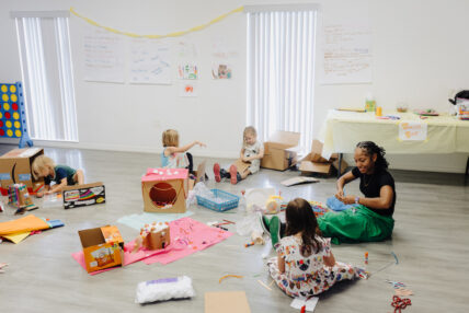 A female teacher surrounded by kids in a classroom doing arts and crafts.