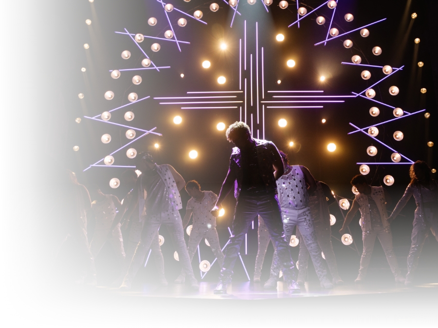 Actors dancing on stage against a neon cross backdrop.