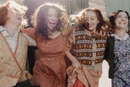 Four actresses smiling with their arms around each other's shoulders.