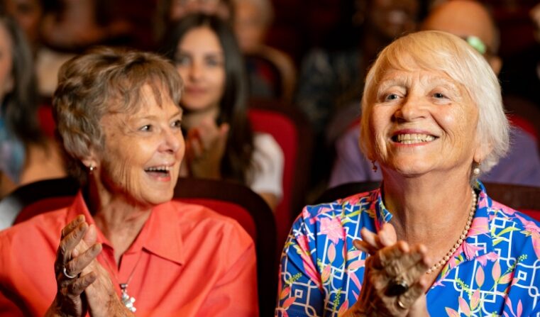 Two elderly women smiling and clapping from the audience.