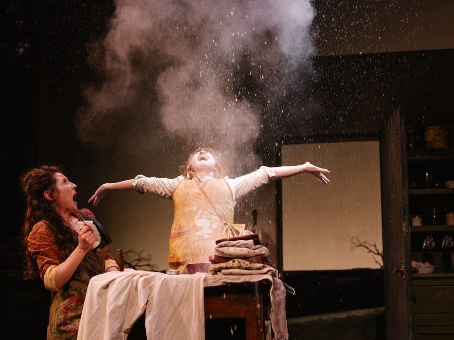 A woman singing and throwing flour into the air while another woman looks at her in shock.