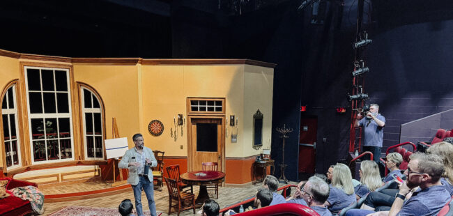 A seated audience looks at a speaker on stage.