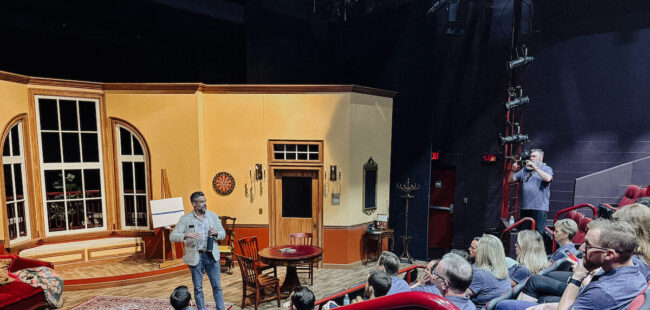 A seated audience looks at a speaker on stage.