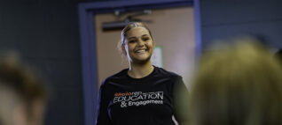 A teen participant of Asolo Rep's high school programming stands in front of a group smiling.