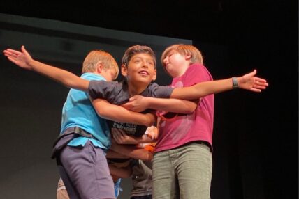 A young boy, held by his friends, acting like he is flying.