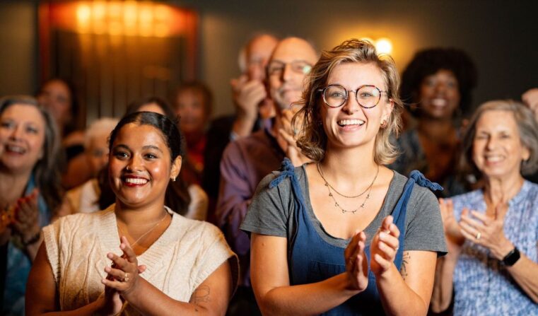 Two women clapping and smiling in a theatre audience.