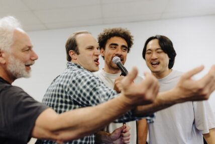 Four men surrounding a microphone and singing.
