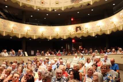 Audience members sitting in a well-lit theatre.