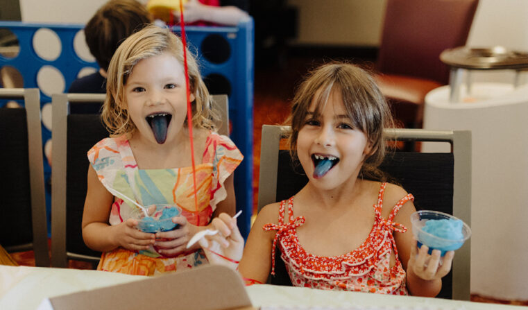 Two little girls stick out their tongues, which have turned blue from a dessert.