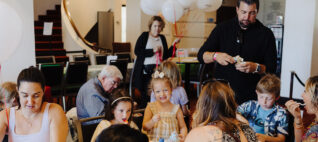 Children and adults seated around a table at an event, eating ice cream.