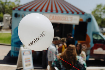 A white balloon on a red string with the text "Asolorep Asolo Repertory Theatre" and a Carousel's food truck parked in the background.