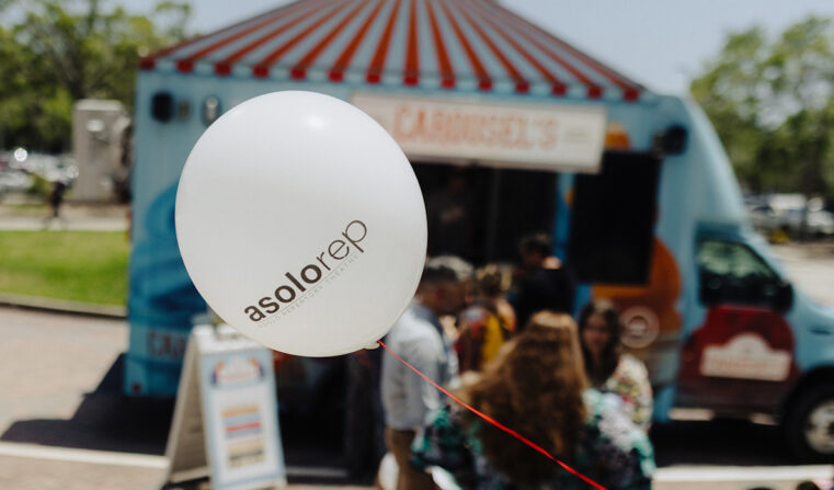 A white balloon on a red string with the text "Asolorep Asolo Repertory Theatre" and a Carousel's food truck parked in the background.
