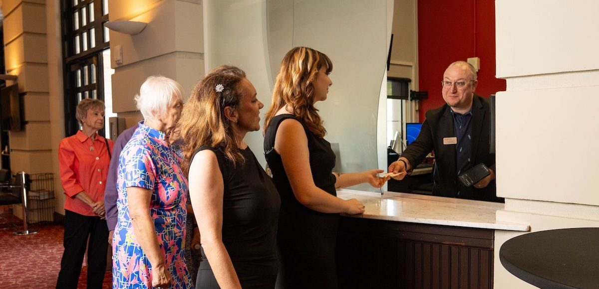 A group of patrons receiving tickets from a box office attendant.