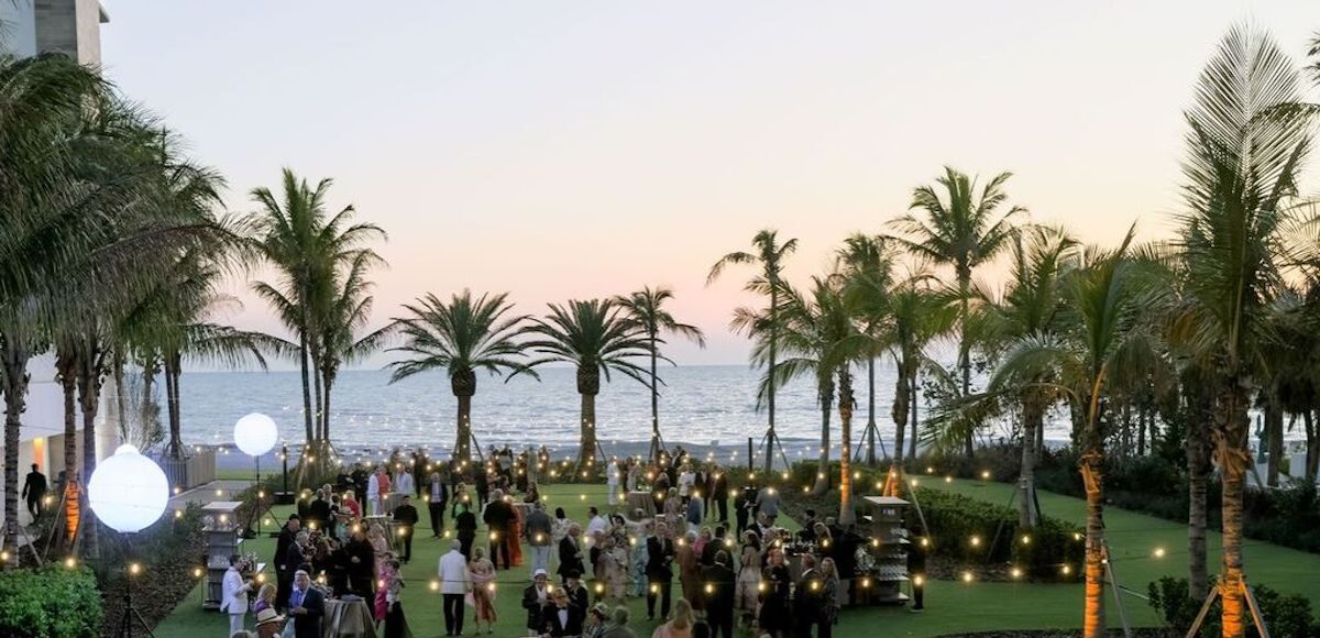 Large group of people attending Asolo Rep's Annual Gala in a grassy area with palm trees and oceanfront view.