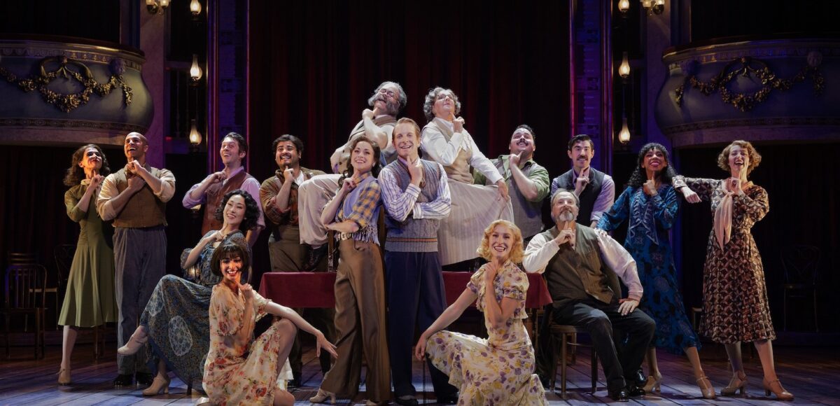 Group of actors dressed in 50/60's clothing posing for a group photo on stage.
