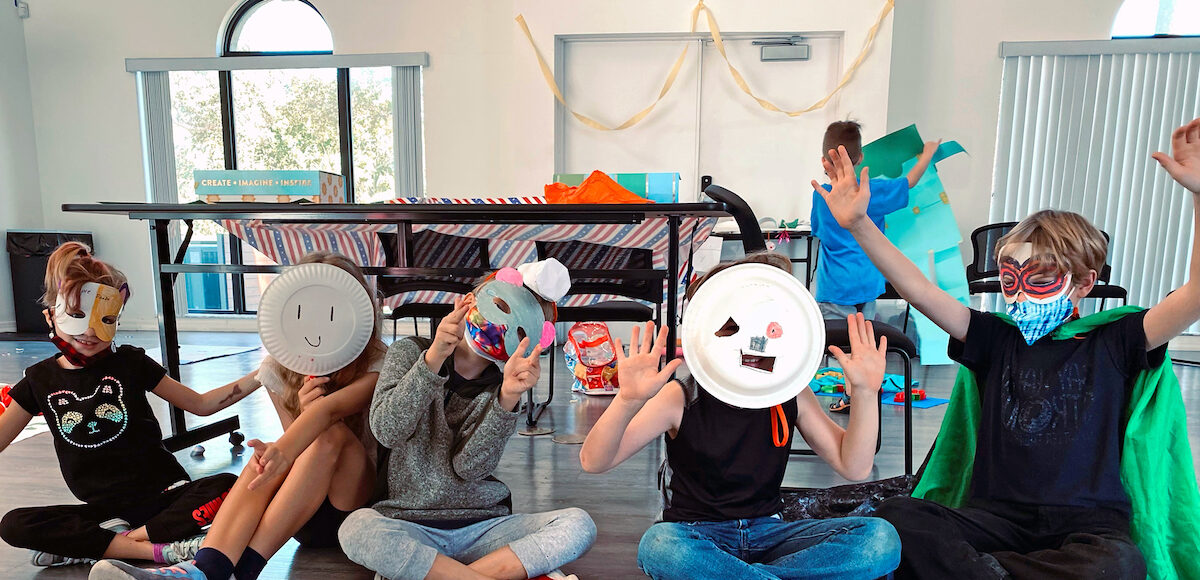 Five kids show off paper plate masks made at a summer camp.