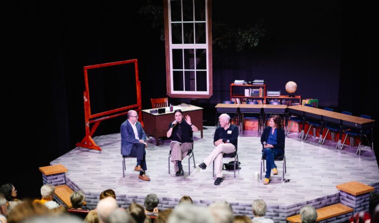 Four people seated in a classroom set, one holding a microphone to speak to the audience.