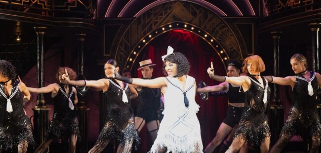dancers in mid-performance wearing black caberet style costumes with the female lead in a white dress