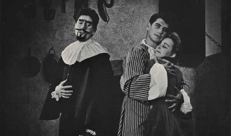 Roxane and Christian de Neuvillette hug as Cyrano looks on, as seen in the play Cyrano de Bergerac.