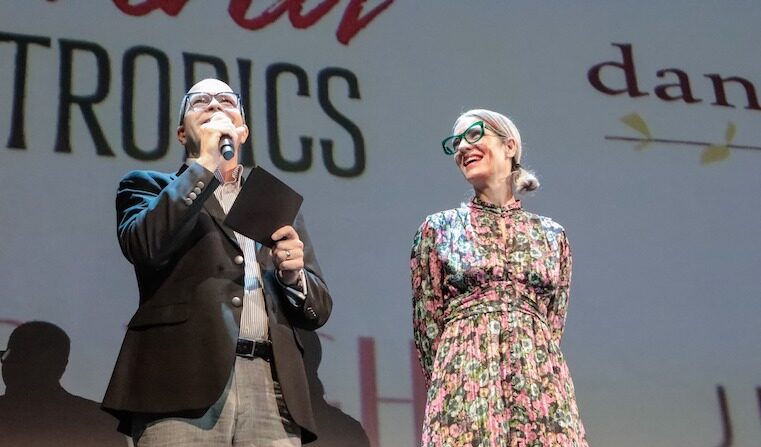 A man and woman stand on stage and speak to the audience.