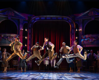 An Asolo Rep performance with male dancers in mid-jump and acting spectators watching.